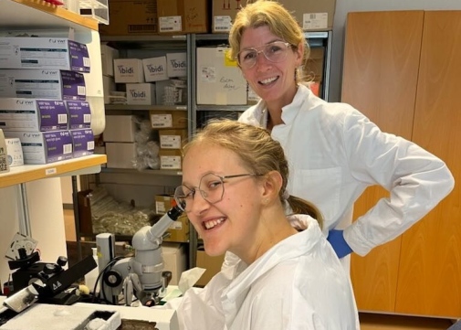 Hedvig i vit labbrock sitter ner, bakom henne står Eva Hedlund, också i labbrock.